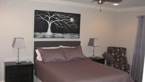 Une chambre bien rangée, avec un grand lit, deux tables de chevet, une chaise et un ventilateur de plafond.
