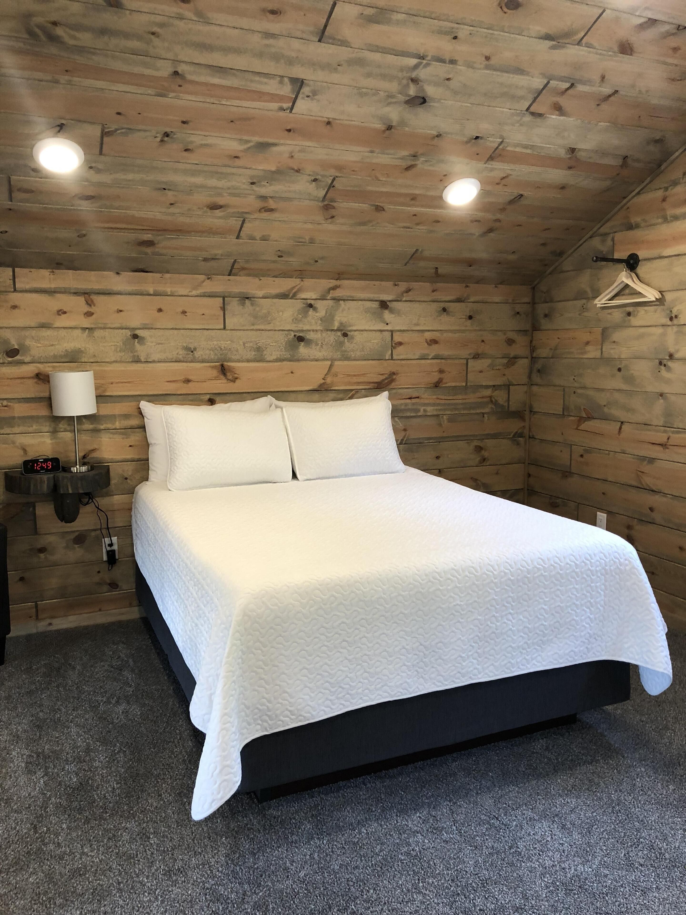 Une chambre à coucher avec un plafond en bois, un lit avec une literie blanche, une table de chevet avec une lampe et une horloge.