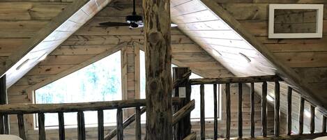A wooden interior with a high ceiling, a wooden staircase, and a ceiling fan.