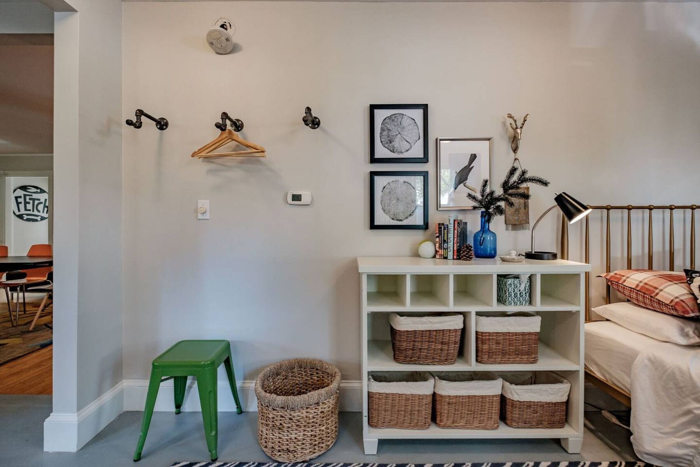 A neatly organized room with a white shelf unit, wicker baskets, a green stool, and wall-mounted decorations.