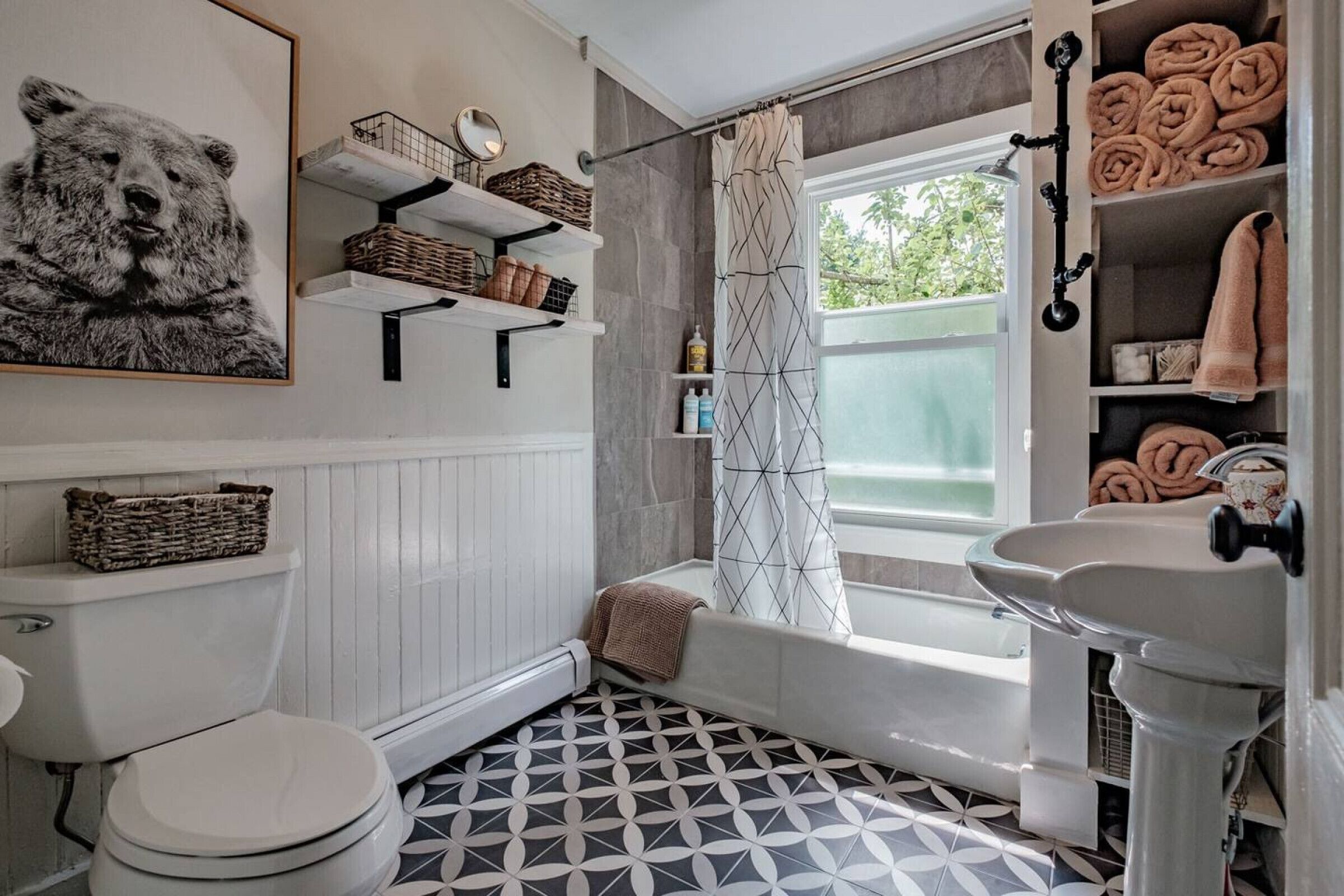 Een badkamer met een patroon vloer, een toilet, een badkuip, een wastafel, planken met handdoeken en een beren kunstwerk aan de muur.