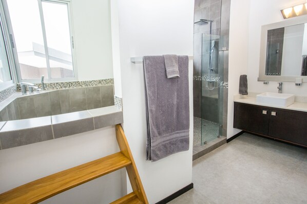 A modern bathroom with a glass shower, a wooden shelf, and a large mirror.