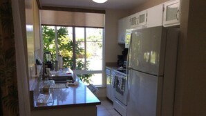 A kitchen with a refrigerator, oven, and a window with a view of greenery. - Amazing Kauai 2 BR Condo Ocean View (Princeville)