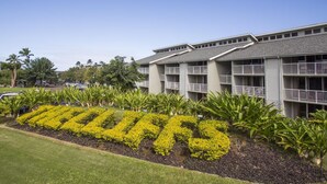 A hotel with a large sign spelling "TRILLO" in yellow flowers, surrounded by well-maintained lawns and tropical plants. - Amazing Kauai 2 BR Condo Ocean View (Princeville)