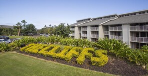 A hotel with a large sign spelling "TRILLO" in yellow flowers, surrounded by well-maintained lawns and tropical plants. - Amazing Kauai 2 BR Condo Ocean View (Princeville)