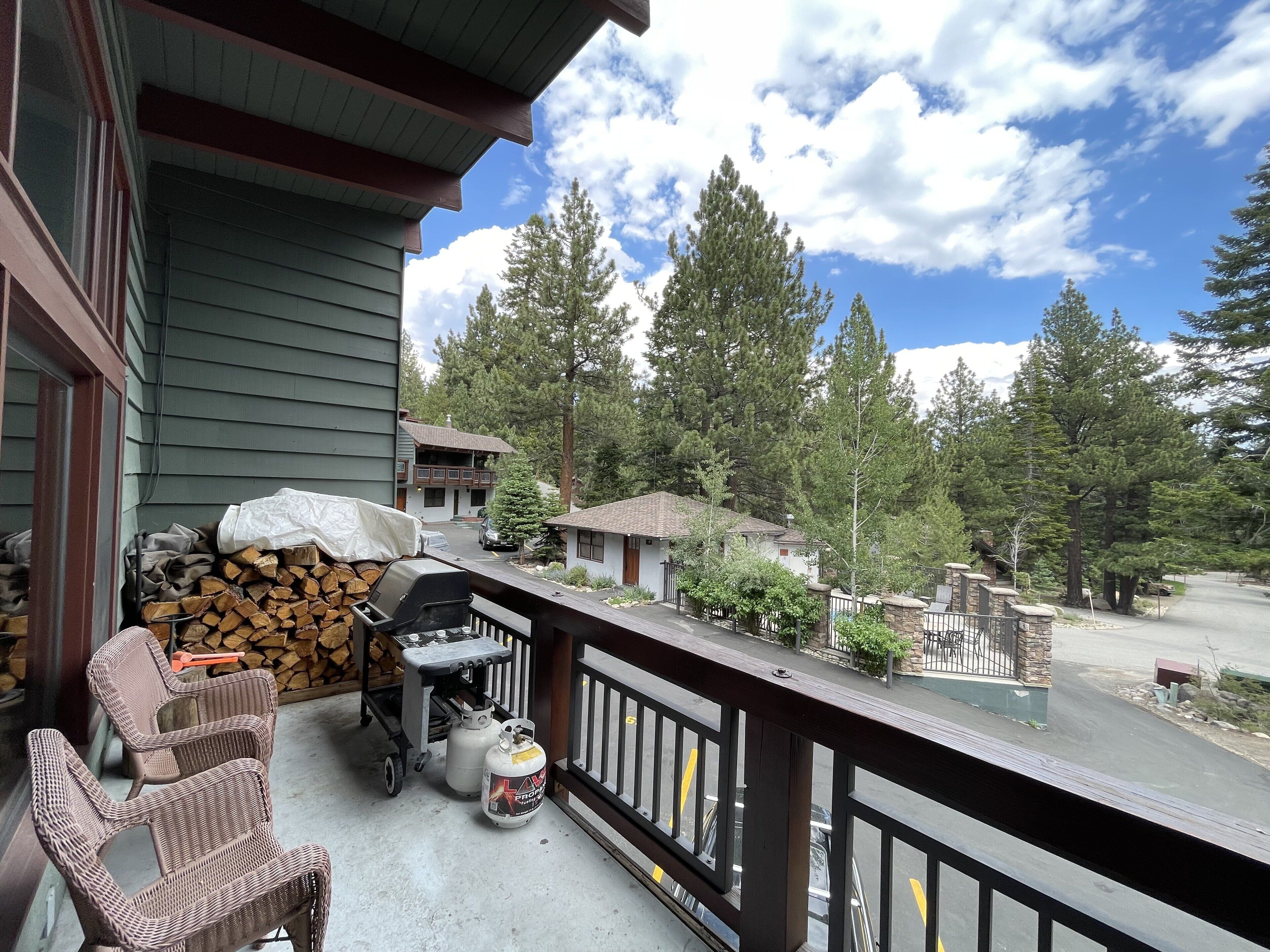 A balcony with wicker chairs, a grill, propane tanks, and a stack of firewood.