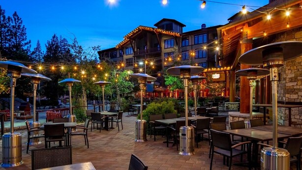 Un espacio al aire libre con mesas y sillas, luces colgantes y un edificio al fondo.