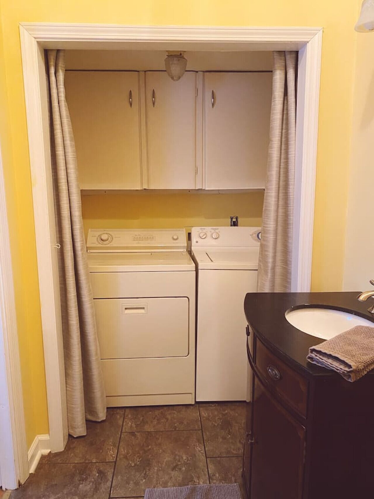 A compact laundry room with a washing machine and dryer, a sink with a towel, and a door with curtains.