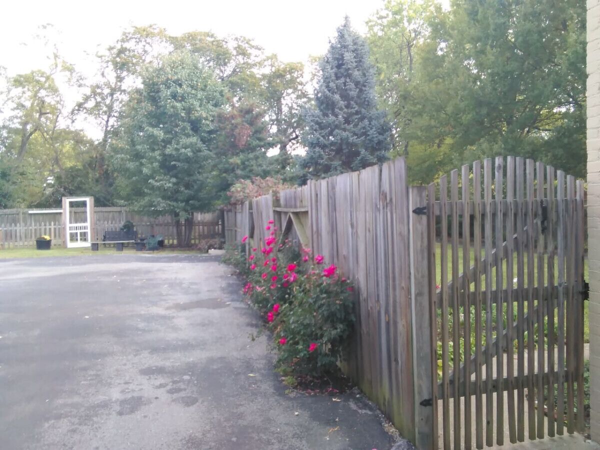 Un camino de entrada cerrado por una valla de madera, un banco y un pequeño edificio al fondo.