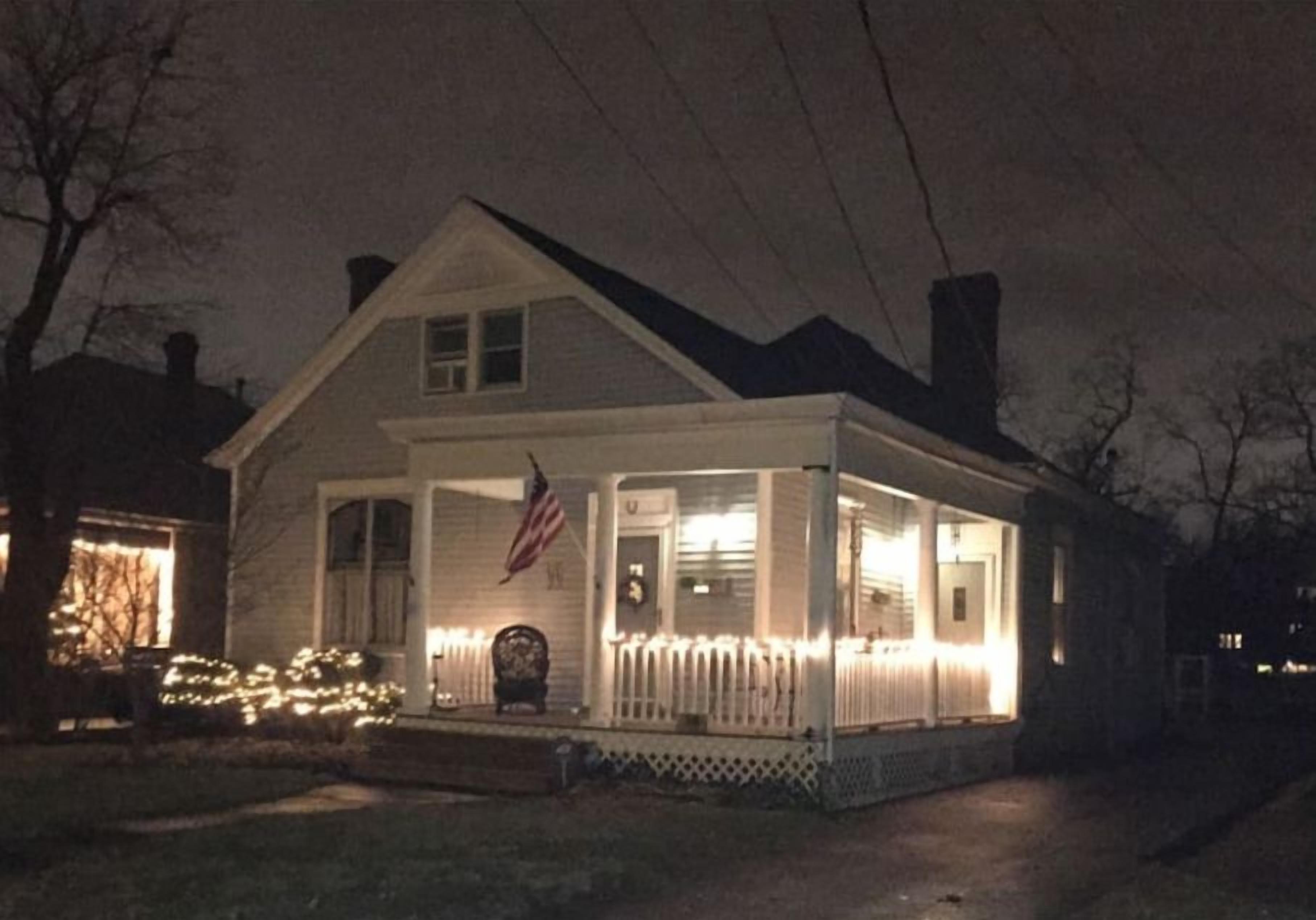 Una casa de dos pisos con porche, una bandera y luces.