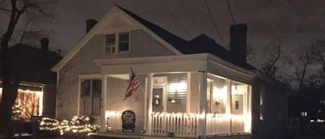 Une maison à deux étages avec un porche, un drapeau et des lumières.