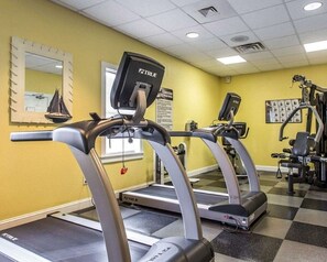 Un gimnasio con cintas de correr, máquinas de ejercicio y un espejo en la pared.