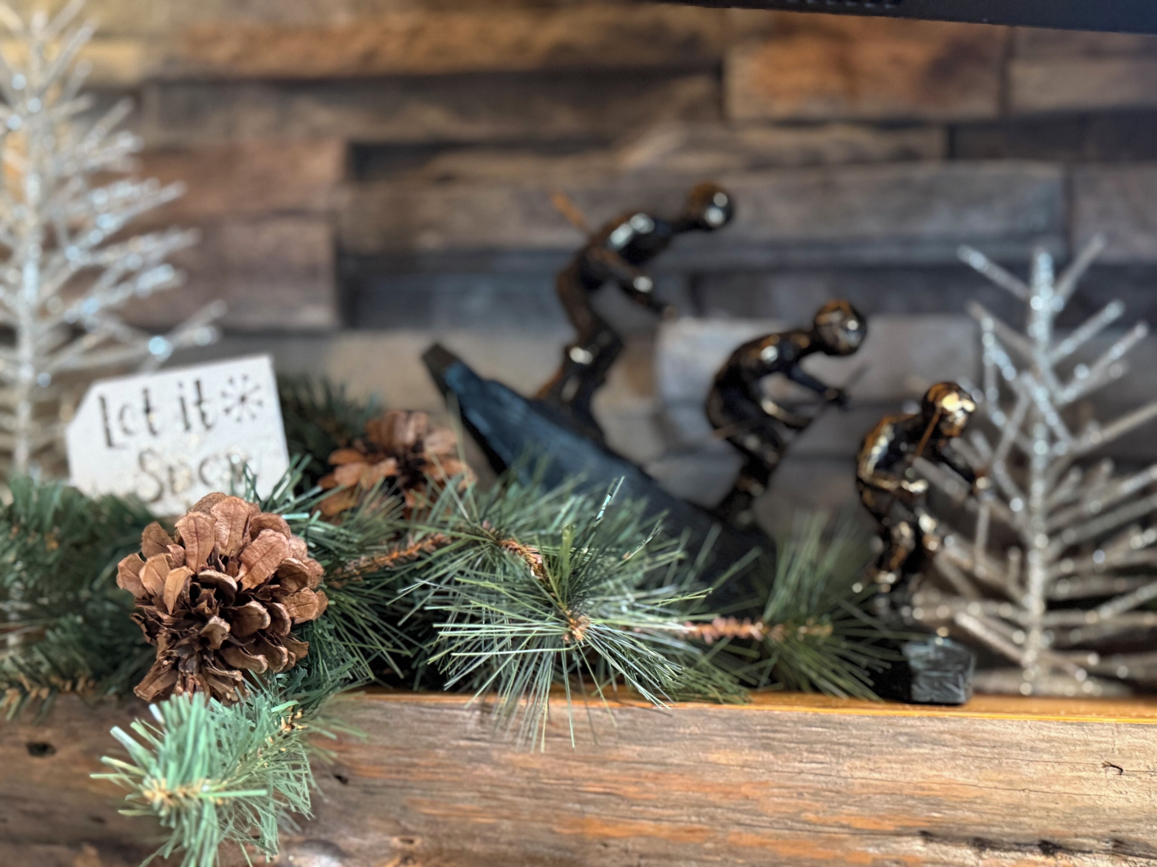 A rustic wooden shelf with pine branches, pine cones, and decorative metal figures.