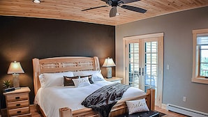 Ein Schlafzimmer mit Holzkopfteil, einem Bett mit weißer Bettwäsche, zwei Nachttischlampen, einer Bank und einem Deckenventilator.