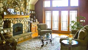 A cozy living room with a stone fireplace, comfortable seating, and large windows allowing natural light. - Newly Built 3 Story Home with Beach Parking Pass (Montauk)