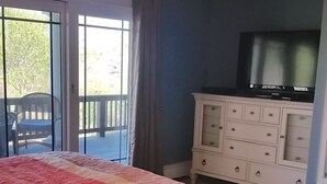 A bedroom with a large bed, a ceiling fan, a TV, and a view of the outdoors through a sliding glass door. - Newly Built 3 Story Home with Beach Parking Pass (Montauk)