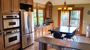 A kitchen with a stainless steel refrigerator, double ovens, a dining table with chairs, and a chandelier. - Newly Built 3 Story Home with Beach Parking Pass (Montauk)