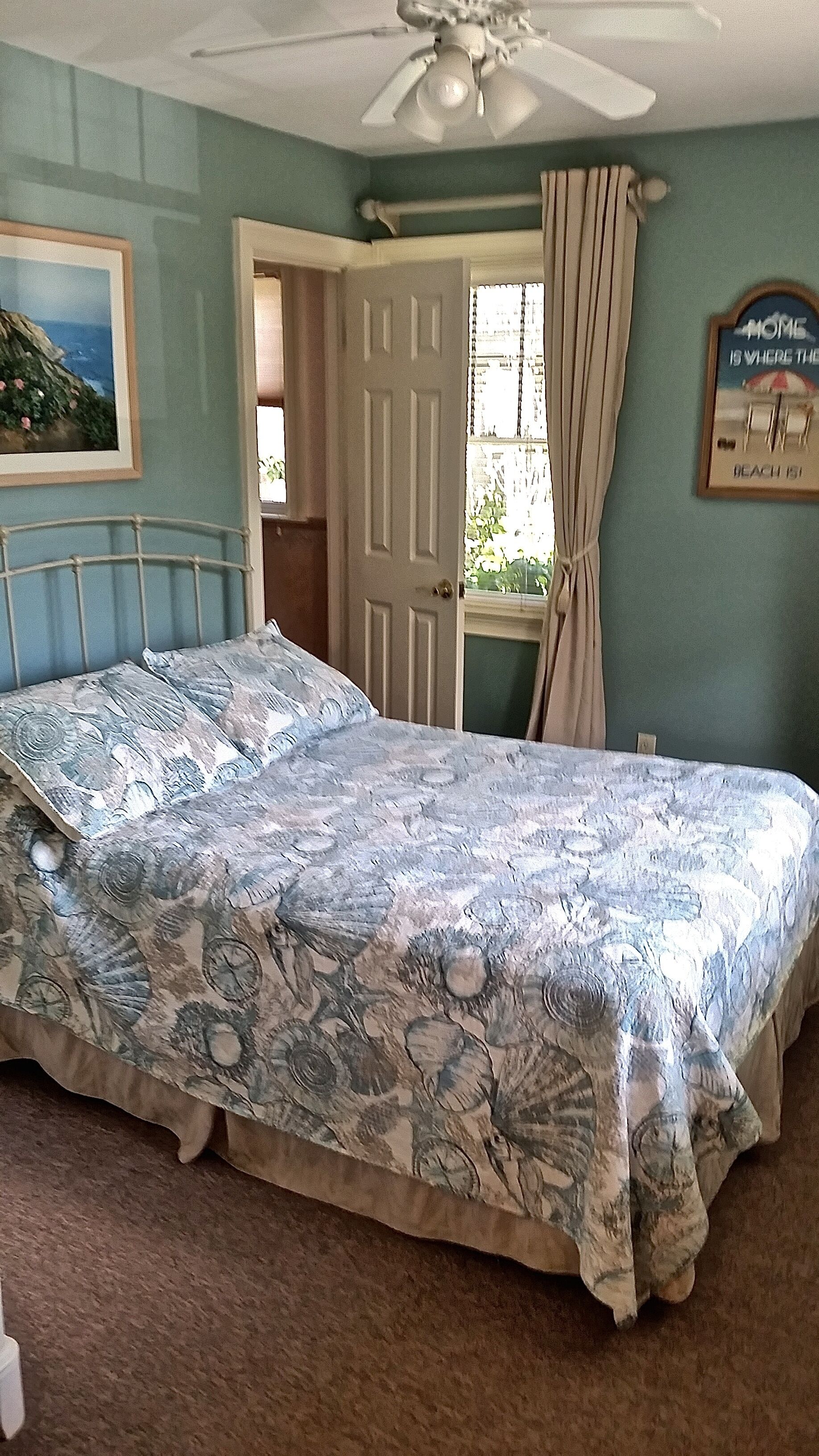A bedroom with a bed, a ceiling fan, a window with curtains, and a door leading to another room.