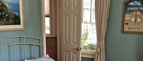 A bedroom with a bed, a ceiling fan, a window with curtains, and a door leading to another room.