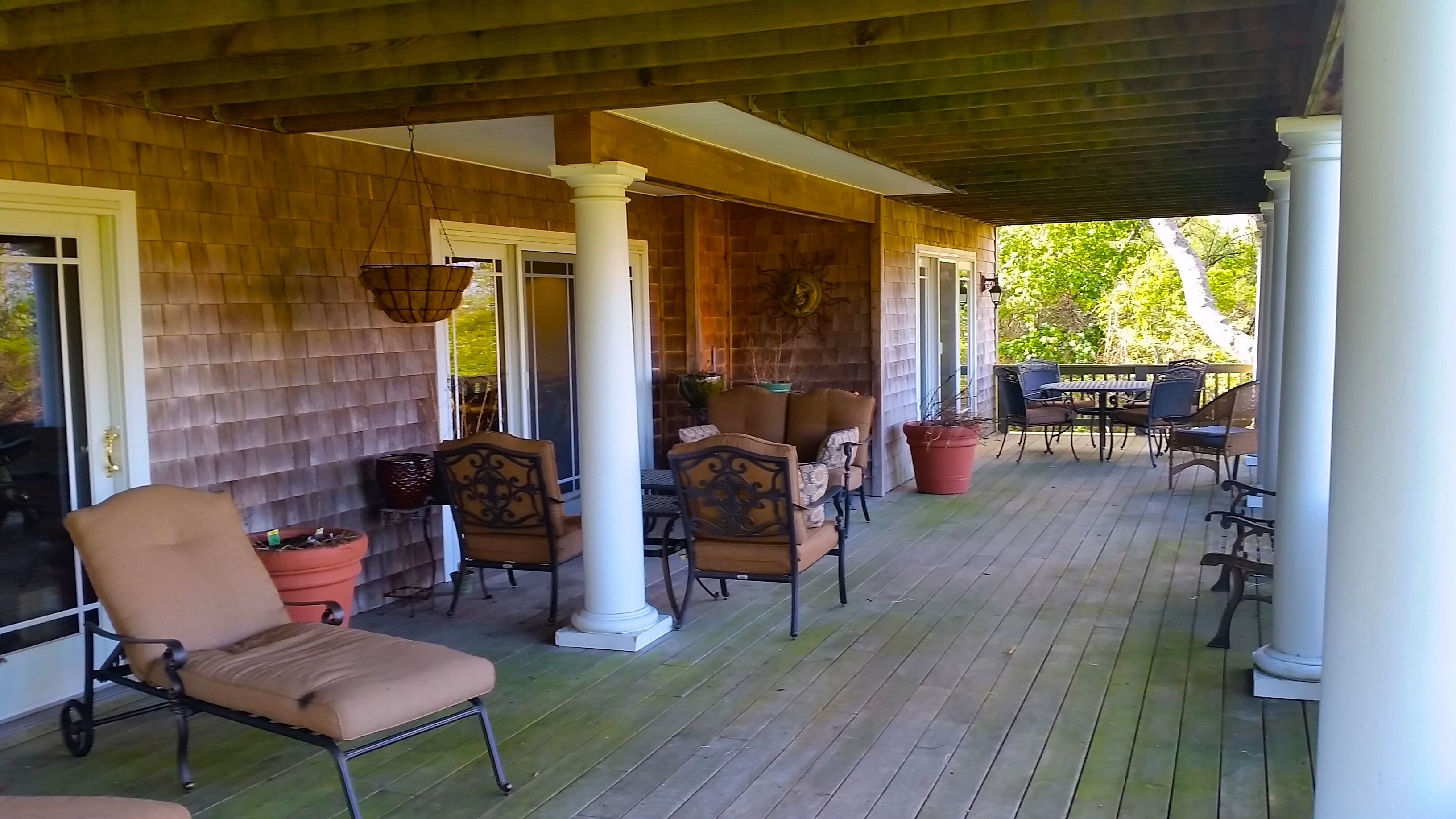 A covered porch with wooden flooring, white columns, and outdoor furniture including chairs and a table.