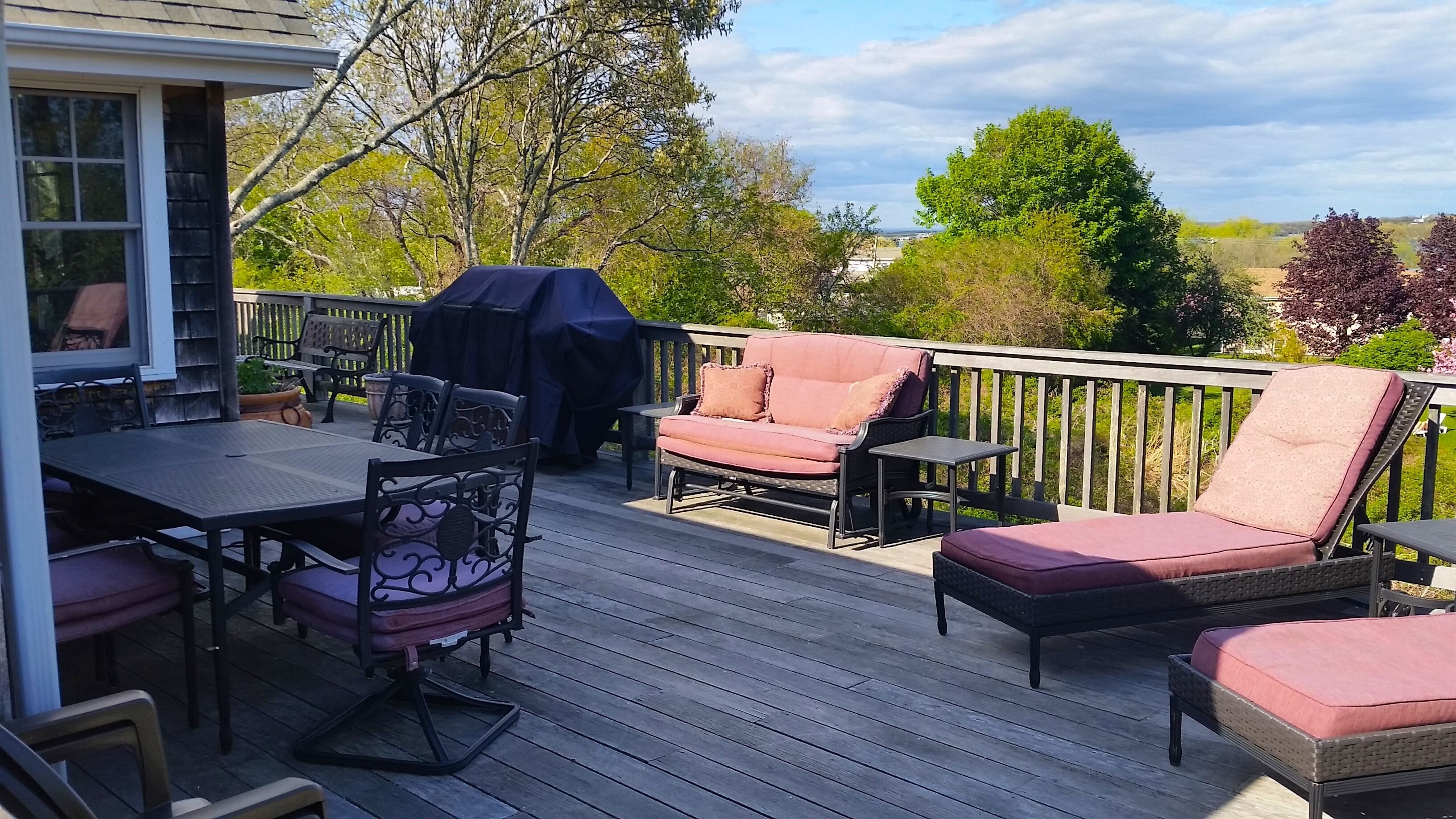 Une terrasse en bois avec mobilier d’extérieur, comprenant une table, des chaises et un espace barbecue abrité.
