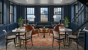 A spacious lounge area with a dark blue wall, large windows, a leather sofa, round tables, and chairs. - Element by Marriott Detroit at The Metropolitan (Detroit)