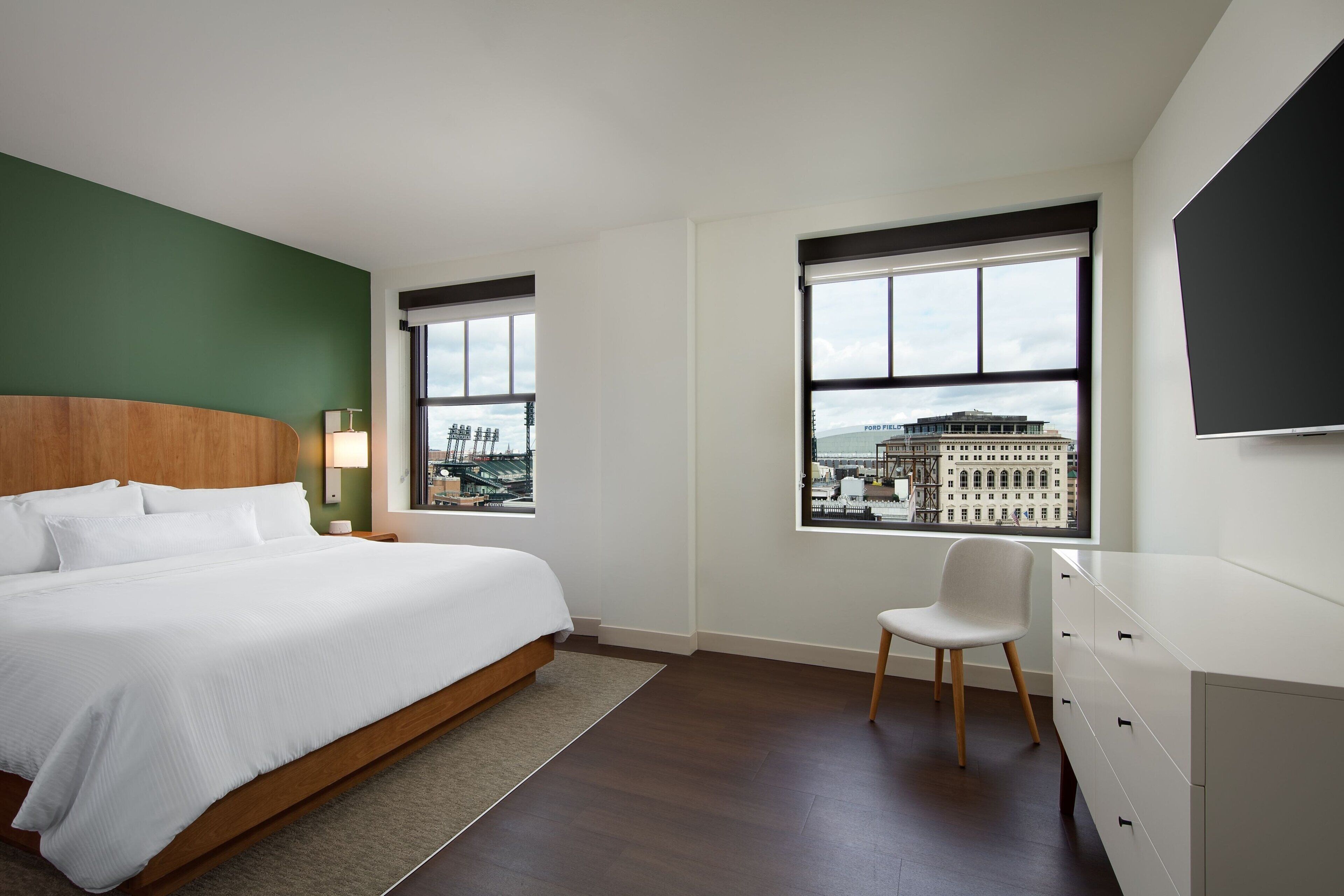 Una habitación de hotel moderna con una cama grande, un escritorio, una silla y vistas a la ciudad.