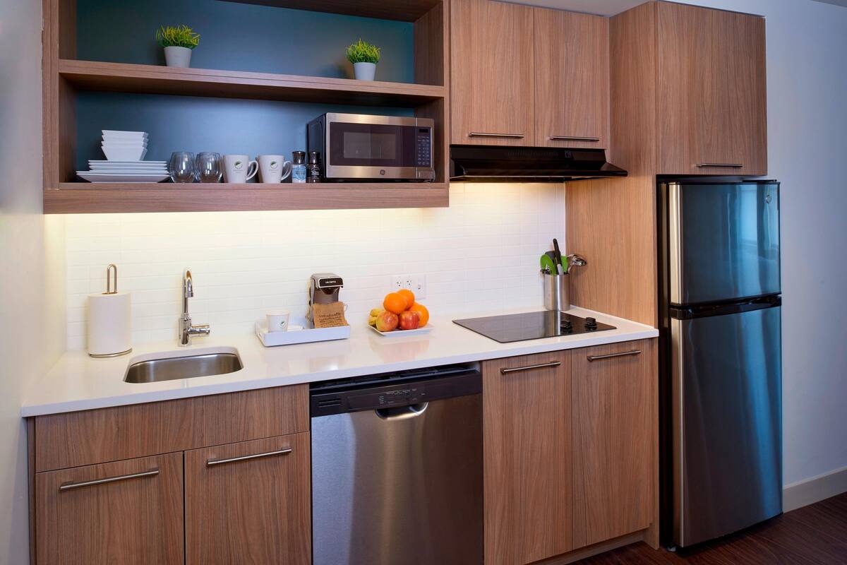 A modern kitchen with wooden cabinets, a stainless steel dishwasher, a microwave, and a refrigerator.