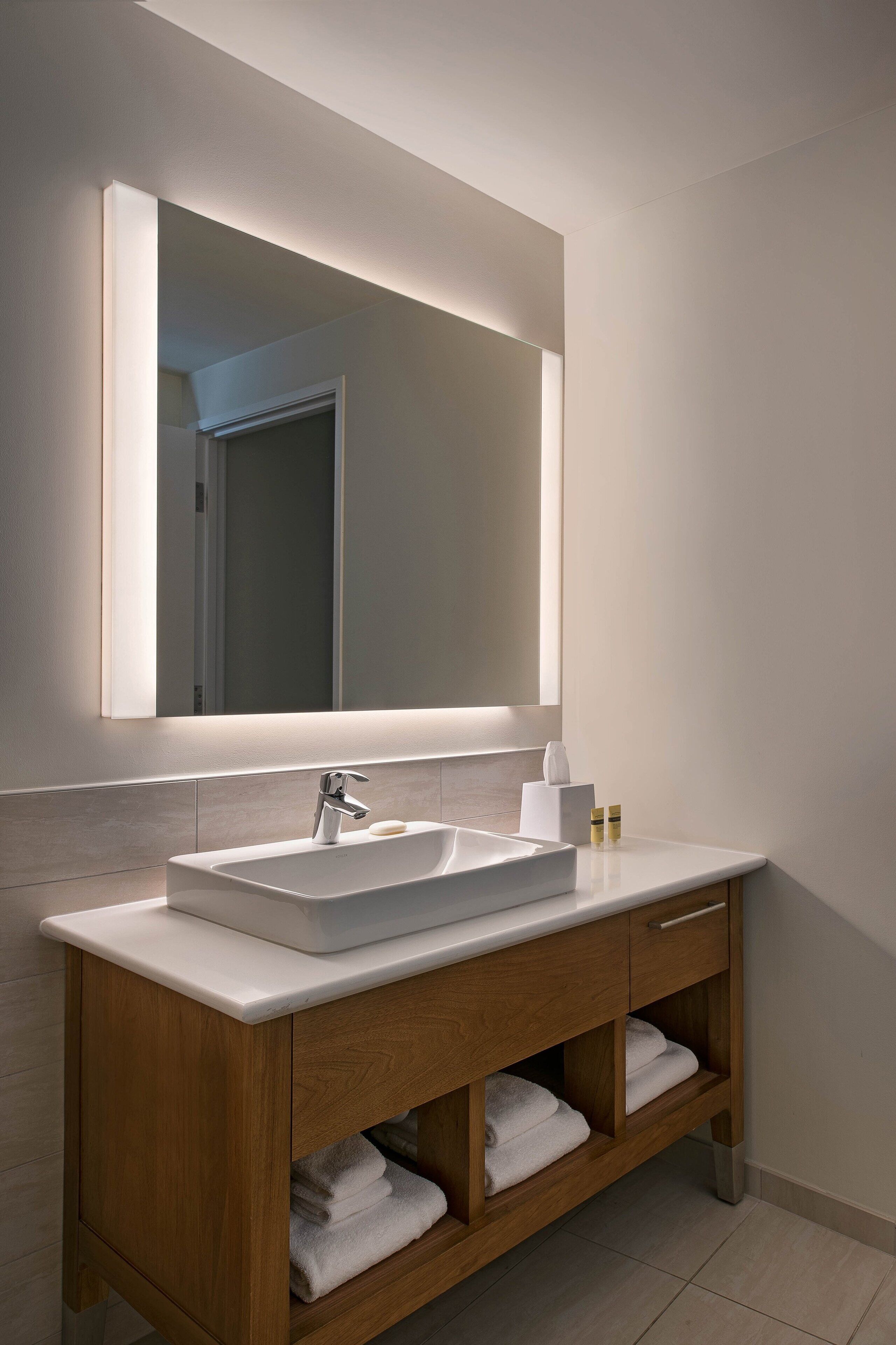 Une salle de bain moderne avec un lavabo blanc, un meuble-lavabo en bois et un grand miroir.
