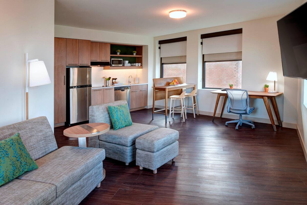 A compact living space with a kitchenette, a dining area, and a seating area with a sofa and ottoman.