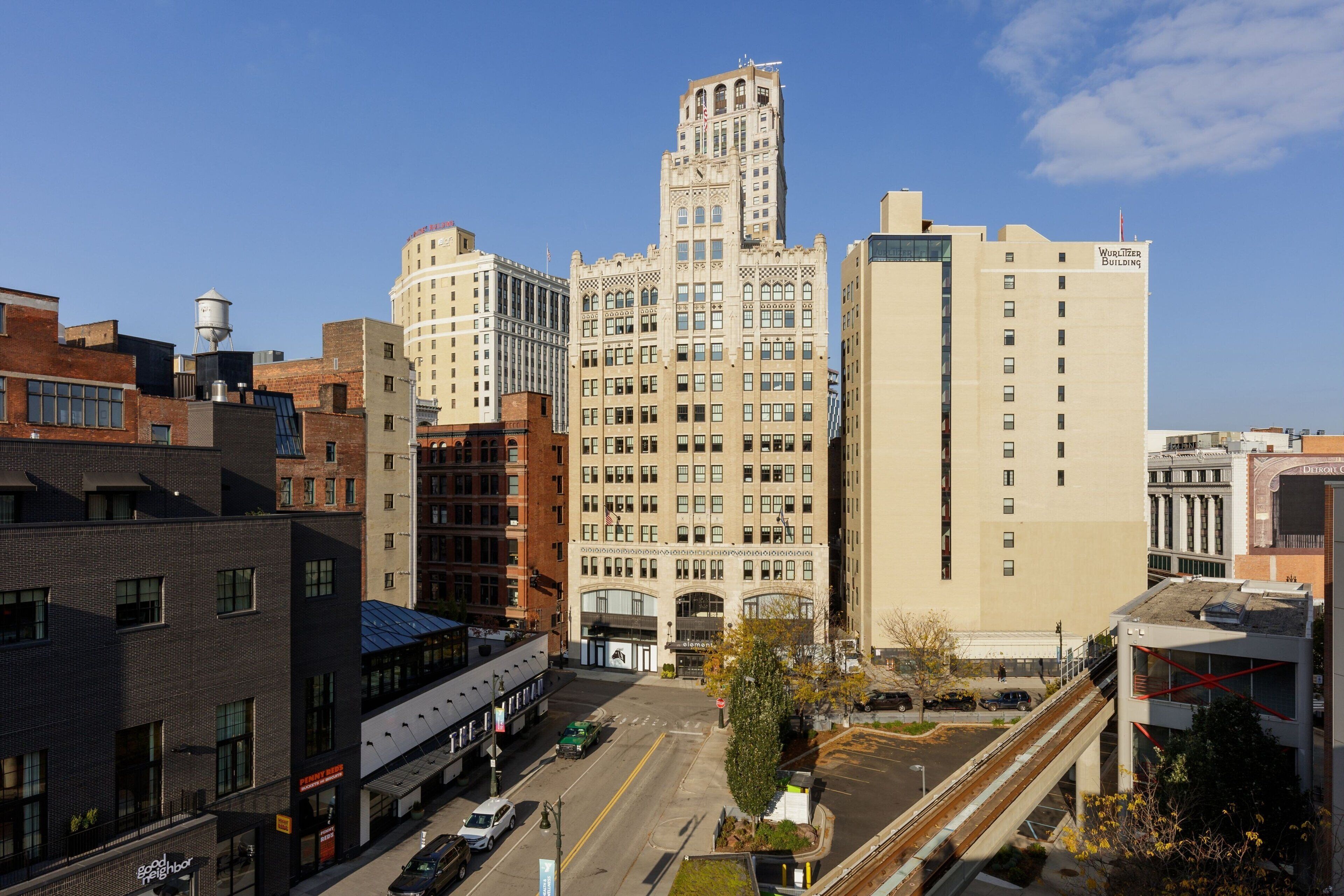 A multi-story building with a prominent tower, a water tower, and a parking lot with vehicles.