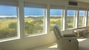A room with large windows offering a view of the ocean and grassy landscape. - Pacific Dreams Beach House- Beach front! Gorgeous views! Meticulously sanitized! (Grayland)