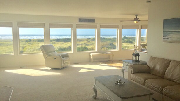 A living room with a view of the ocean, a white leather sofa, a white armchair, and a small table. - Pacific Dreams Beach House- Beach front! Gorgeous views! Meticulously sanitized! (Grayland)