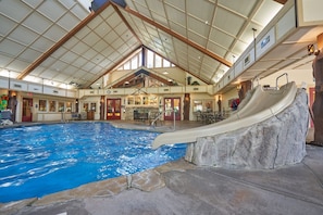 An indoor swimming pool with a slide, wooden beams, and a stone feature. - Wilderness Club™ at Big Cedar® - 2 Bedroom Combined Lodge (Ridgedale)