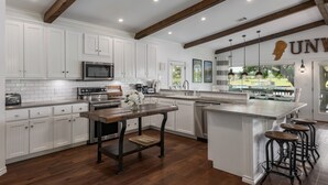 A modern kitchen with white cabinets, a wooden island with stools, and a view of the outdoors through large windows.