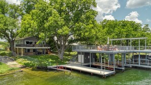 A waterfront property with a dock, a covered outdoor seating area, and a house with a balcony overlooking the water.