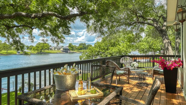 A deck with wicker furniture, a table with bottles, and a view of a lake and trees.