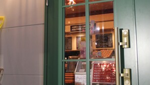 A green door with a glass panel, a light fixture above it, and a doorbell.