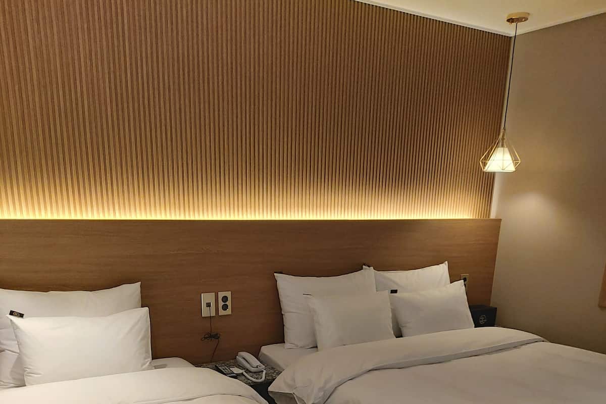 A hotel room with two beds, a wooden headboard, a bedside telephone, and a pendant light.