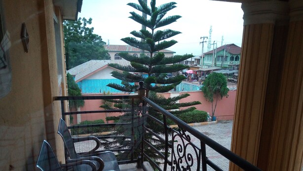 Un balcón con sillas de metal y barandilla que da a un patio con árboles y edificios.