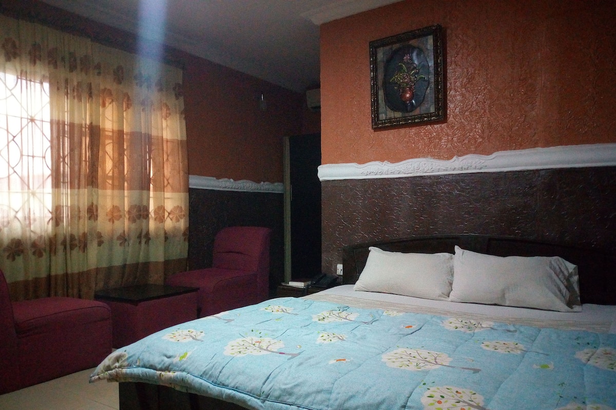 A bedroom with a bed, a chair, a TV, and a painting on the wall.