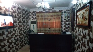 Una zona de recepción con mostrador de check-in, paredes con diseño, ventilador de techo y un cuadro en la pared.