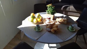 Een ronde eettafel met diverse soorten eten, zoals fruit, brood en gebak, op een witte tafelkleed.