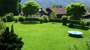 Ein grüner Innenhof mit einem Brunnen, umgeben von Bäumen und Gebäuden mit geneigten Dächern.