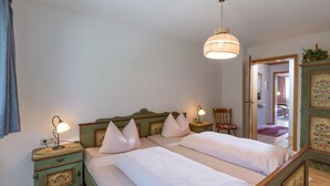 Ein Schlafzimmer mit einem Doppelbett, zwei Nachttischen, einer Hängeleuchte, einem Sessel und einer Tür zu einem anderen Raum.