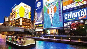 Zona urbana iluminada con carteles luminosos y un barco en el agua.