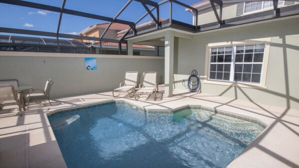 A swimming pool with lounge chairs and a hose reel, surrounded by a covered patio area.
