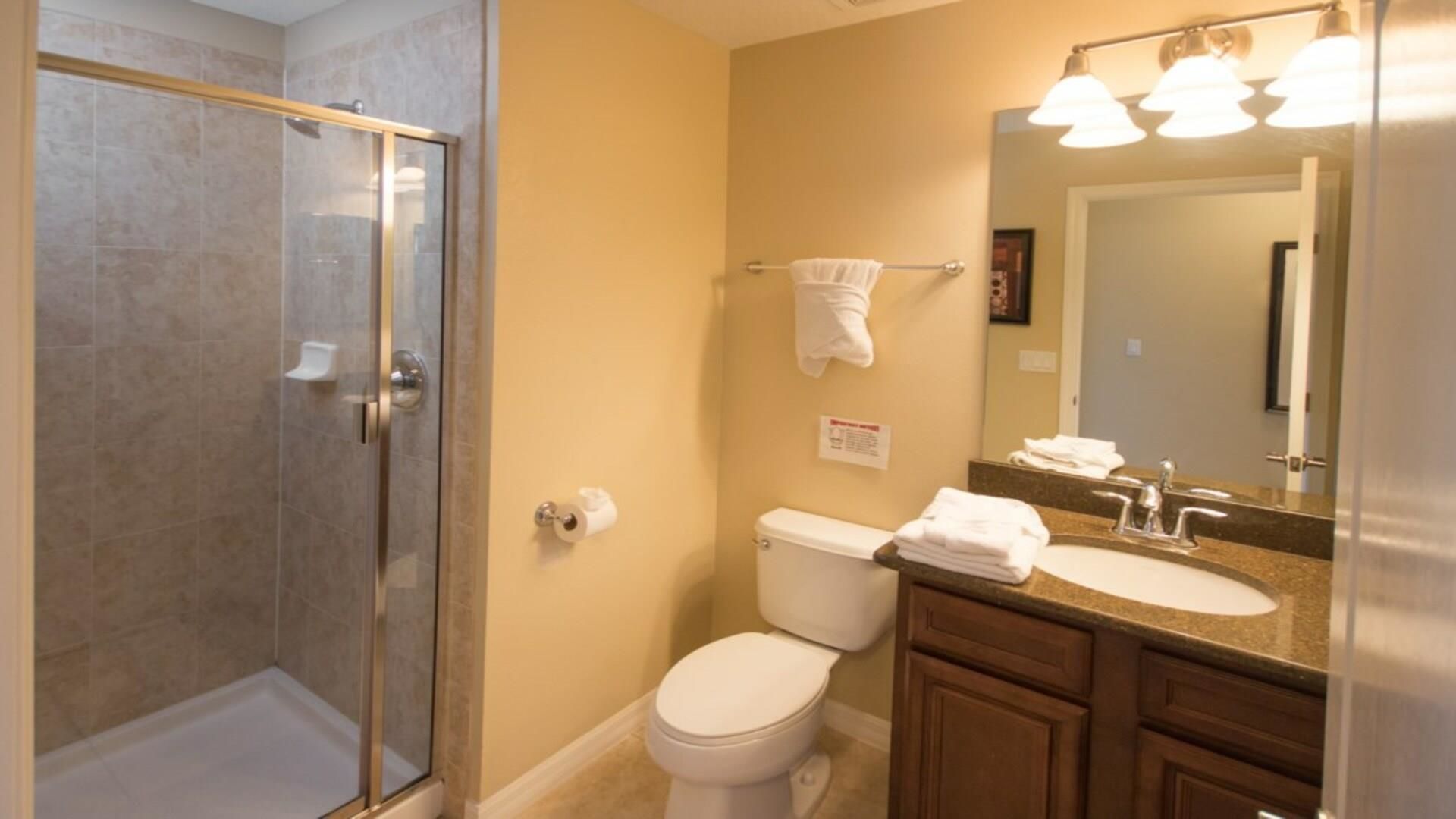 A bathroom with a glass-enclosed shower, a toilet, a sink with a mirror, and a towel rack.