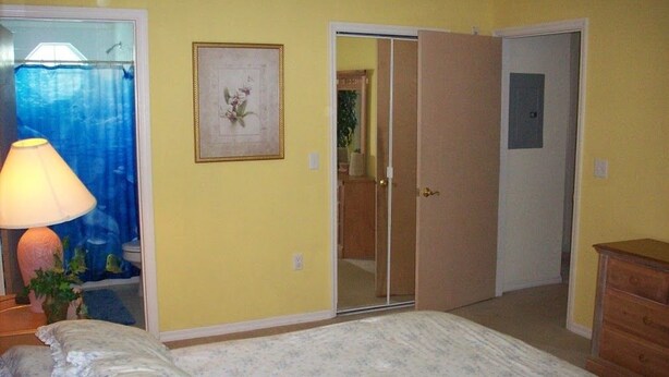 Un dormitorio con cama, lámpara, cómoda y puerta que da a otra habitación.