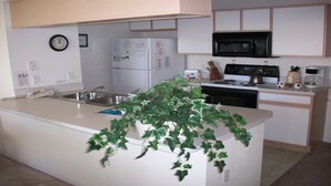 Una cocina con una isla central, microondas, estufa, refrigerador y un reloj en la pared.